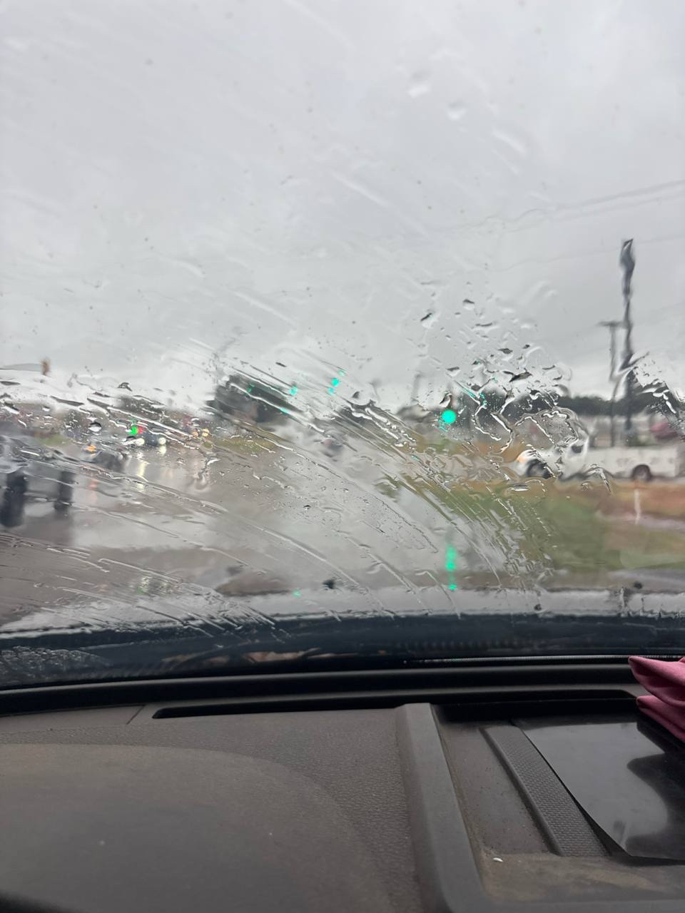 Rain blurs a view through a car windshield at a traffic light on a gray day.